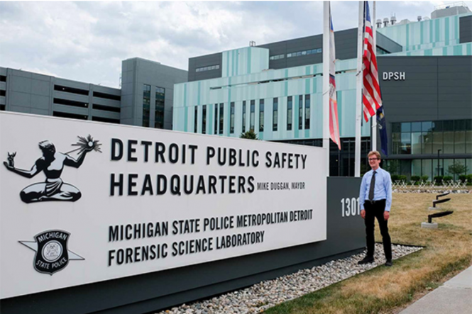 Reid Wilson standing outdoors in front of sign: Detroit Public Safety HQ