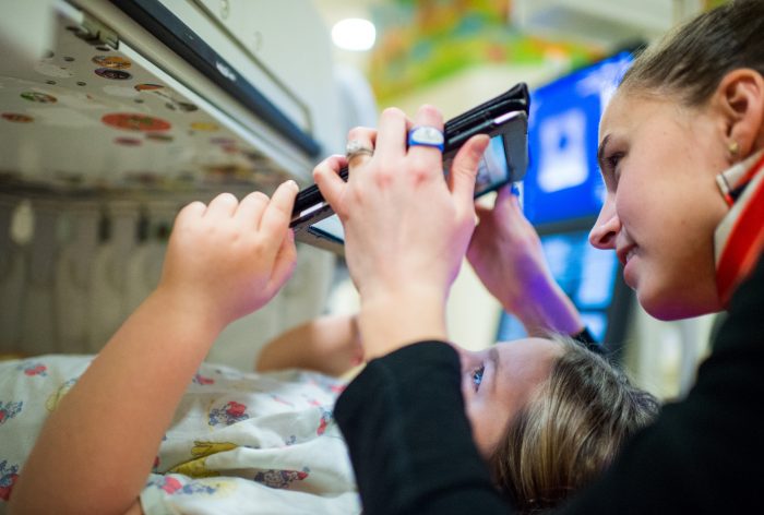 close up of female nurse holding iPad up for viewing by a young patient lying in bed.