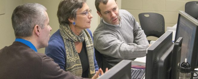 Two men and a women sitting at computer, man gesturing to screen.