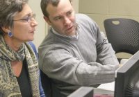 Two men and a women sitting at computer, man gesturing to screen.