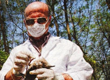 Man in mask and lab coat outdoors, examining captured bird for avian flu.