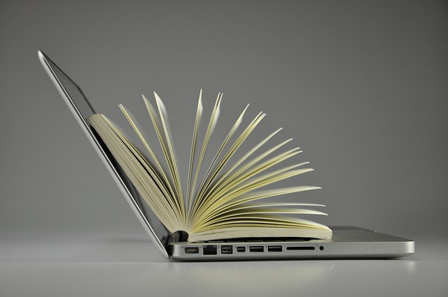 Side view of open laptop with book inside with fanned pages.