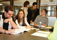 Group of students sitting around a classroom table talking.