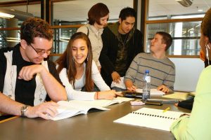 Group of students sitting around a classroom table talking.