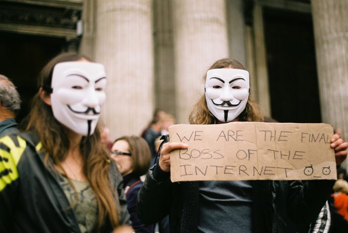 Two masked protesters holding a cardboard sign: We are the final boss of the internet.
