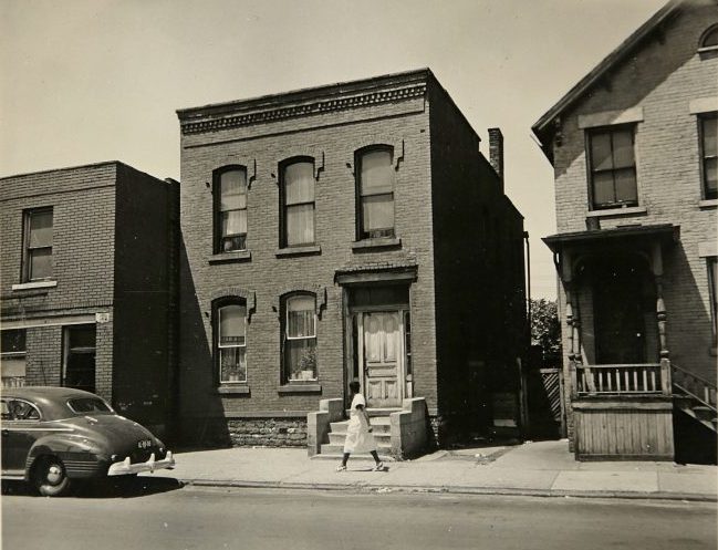 BW photo of woman walking along the street in Detroit's Black Bottom.