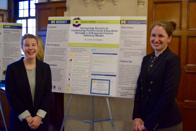 Two women standing next to a poster on a stand.