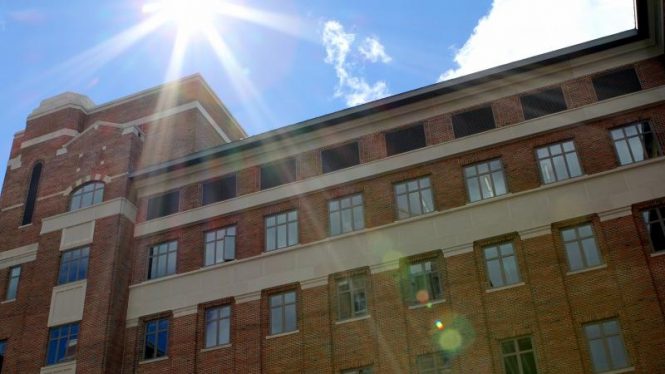 Low angle photo looking up the face of North Quad, sun and sky in the BG.