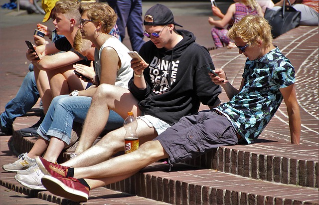 Group of young people sitting on stairs outside, all checking their phones.