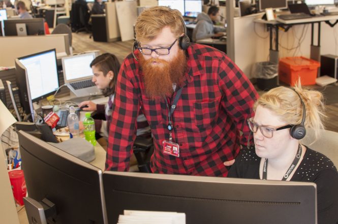 Man and woman at computer desk, wearing headphones and looking at monitors.