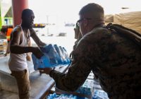 A U.S. Marine helps a civilian airport employee deliver water for distribution