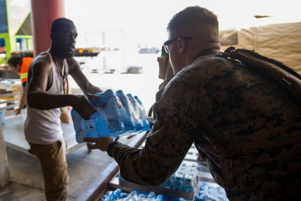 A U.S. Marine helps a civilian airport employee deliver water for distribution