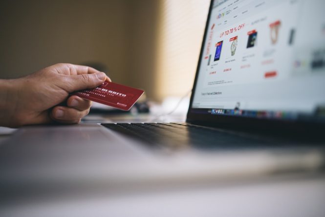 hand holding credit card, laptop in background