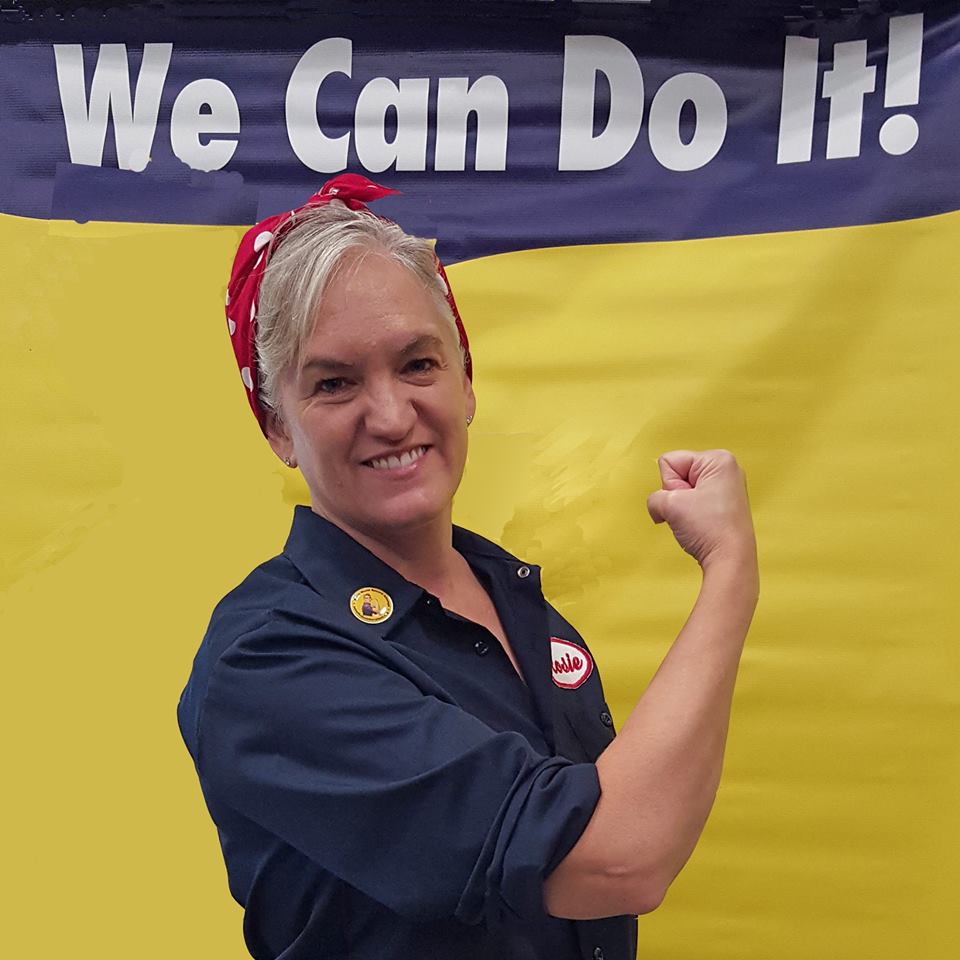 A woman impersonating Rosie the Riveter smiles and flexes her bicep