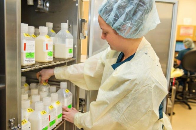 Woman in sanitary scrubs arranging bottles in a refrigeration unit.