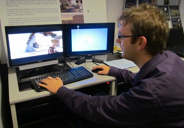 male student playing online game on two computer monitors