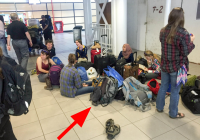 students sitting on floor of airport terminal surrounded by luggage.