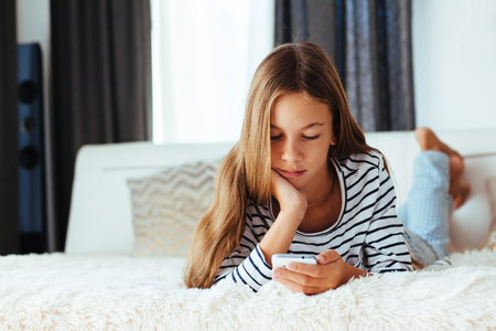 10 years old pre teen girl lying down on sofa and playing with smartphone