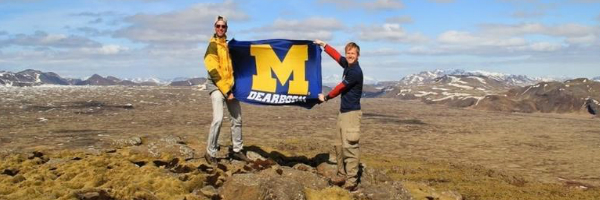two students standing in an open field holding M Dearborn banner