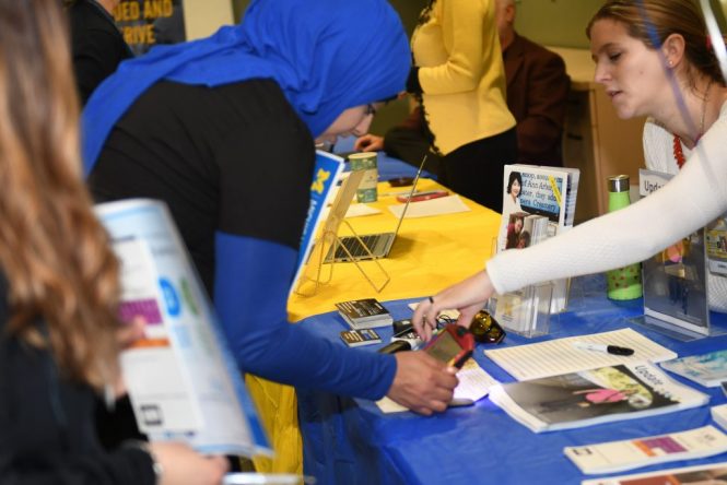 Two women lean over a table to share information.