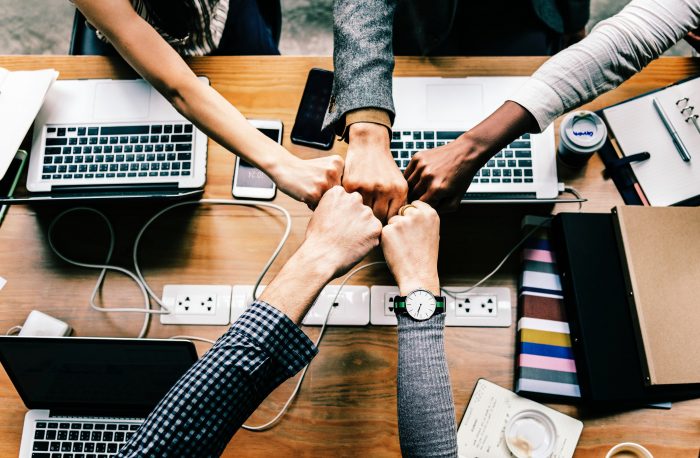 five arms fist bumping over table with various devices