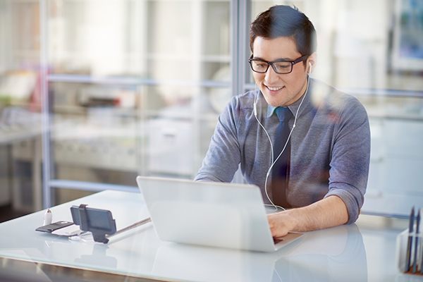 Asian man wearing earbuds, works at compuer