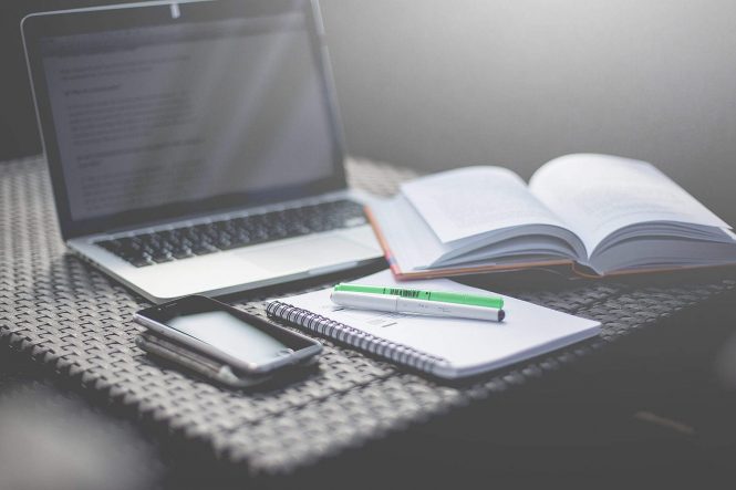B&W photo of laptop, book, notebook, and phone