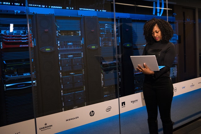 woman holding laptop standing next to server rack