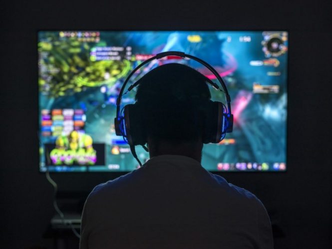 Gamer wearing headphones in front of computer screen.