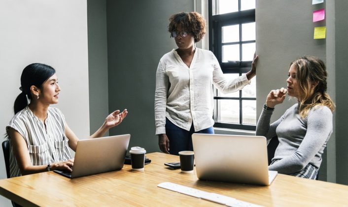 three woman talking in conference room, computers on the table