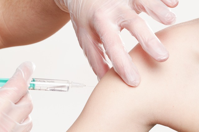 gloved hands inserting hypodermic needle into upper arm