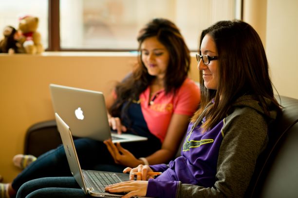 two female students sitting on a sofa using laptops