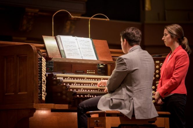 Young man sitting at organ, woman standing next to him.