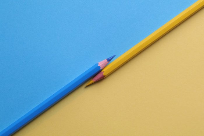 A blue pencil and maize pencil over a blue and maize background.
