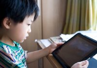 A kid sitting at a desk looking at an iPad