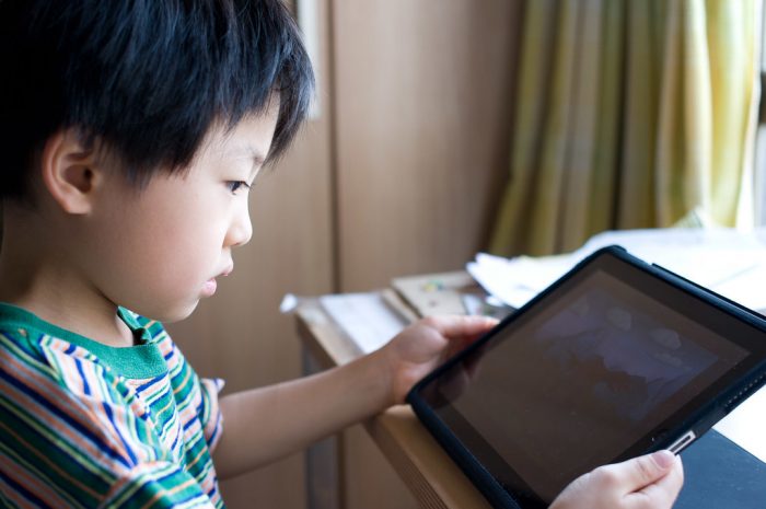 A kid sitting at a desk looking at an iPad