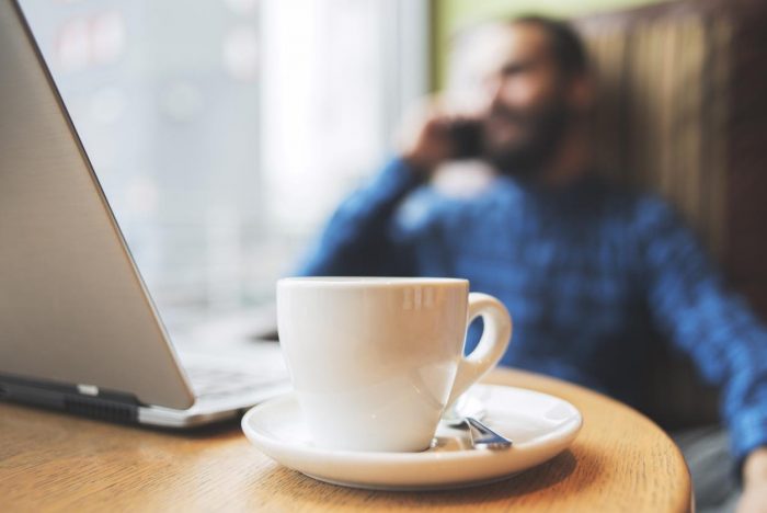 man on phone in cafe with laptop and coffee