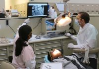 Dentist and hygienist look at monitor, patient in chair.