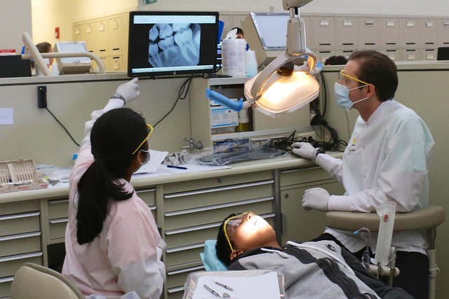 Dentist and hygienist look at monitor, patient in chair.