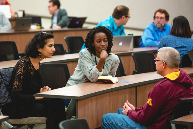 Two women of color and man sitting at desk talking.
