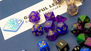 multicolored gaming dice on table next to Gameful Leaning card