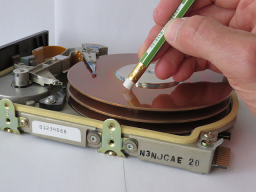 hand holding pencil with eraser over a hard drive