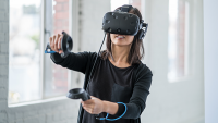 Woman wearing VR/AR goggles, holding controllers.
