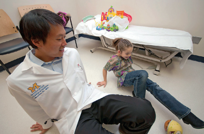 Asian male physician playing with child hospital room.