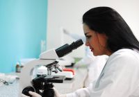 Woman in white lab coat looking through a microscope.