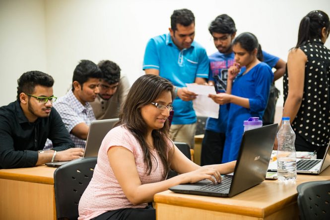 Group of Indian students sitting at tables and working on computers.