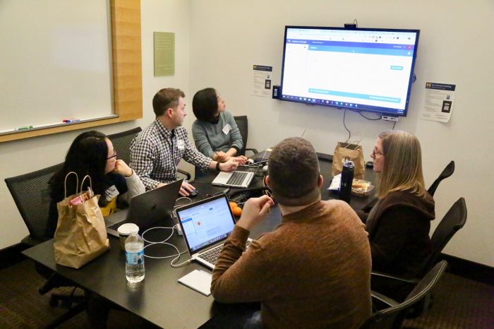 group of people sitting around a table looking at a large display