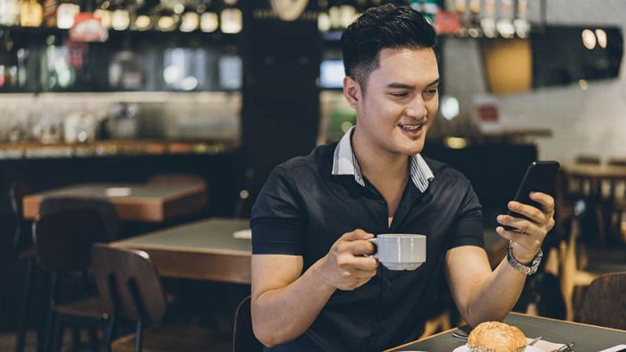 asian man drinking coffee looking at phone