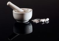 white mortar and pestle on black BG with ground up pills