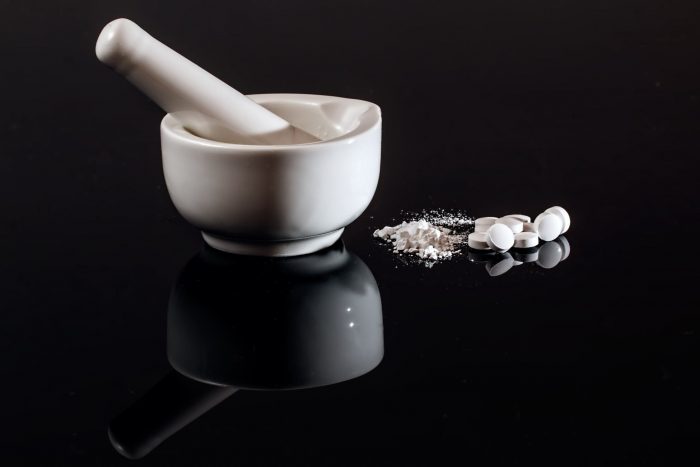 white mortar and pestle on black BG with ground up pills